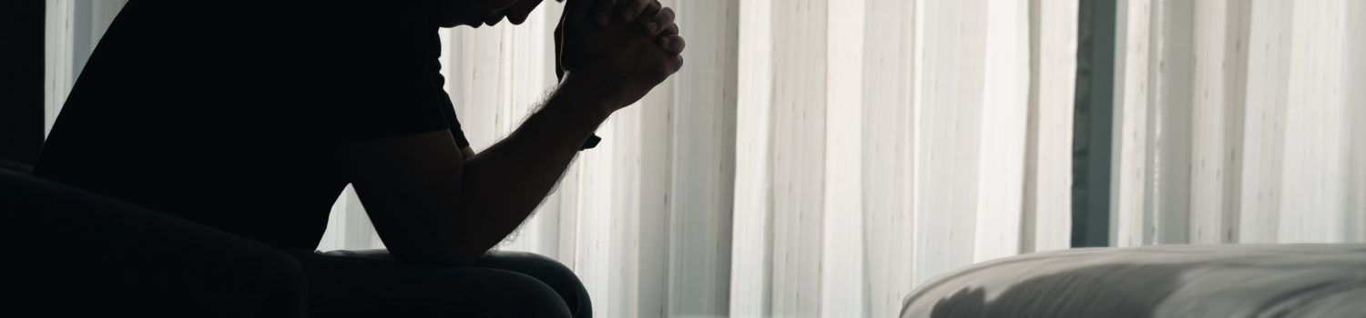 Depressed man sat lonely in a dark room with hands to head